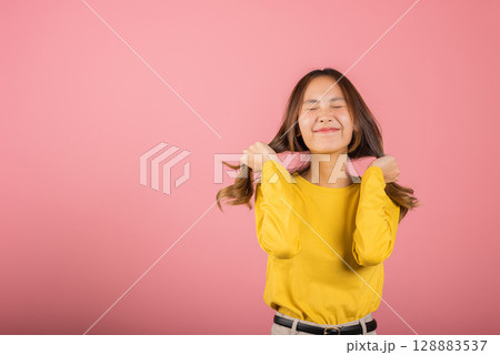 Portrait Asian attractive young woman wearing a yellow shirt with long hair is smiling and holding her hair back in studio shot isolated on pink background, so happy and funny cute girl Portrait Asian attractive young woman wearing a yellow shirt with long hair is smiling and holding her hair back in studio shot isolated on pink background, so happy and funny cute girl 128883537
