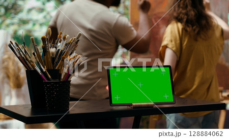 Diverse artists painting new artwork next to isolated mockup screen, collaborating on masterpiece for fine art gallery exhibition. Painter and apprentice using watercolor paints on canvas. Camera A. Diverse artists painting new artwork next to isolated mockup screen, collaborating on masterpiece for fine art gallery exhibition. Painter and apprentice using watercolor paints on canvas. Camera A. 128884062