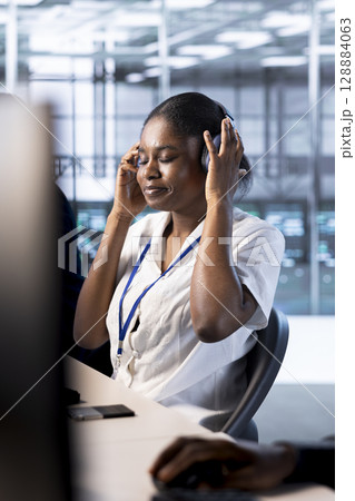 African american admin in data center wearing headphones, enjoying music while running system diagnostic tests. Woman in server hub listening songs, looking for network issues affecting rigs African american admin in data center wearing headphones, enjoying music while running system diagnostic tests. Woman in server hub listening songs, looking for network issues affecting rigs 128884063