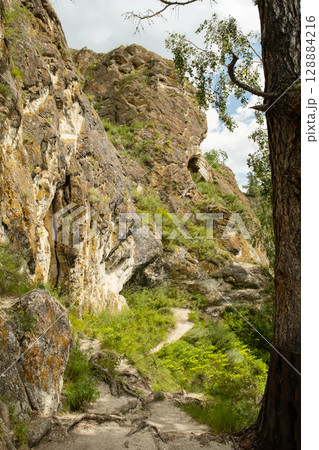 Scenic view of rock formations and a hiking trail winding through lush green vegetation under a cloudy sky. Scenic view of rock formations and a hiking trail winding through lush green vegetation under a cloudy sky. 128884216