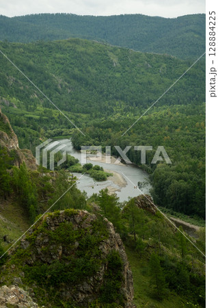 Grand vista of a winding river flowing through a lush green valley with many trees. 128884225