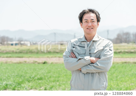 田舎の田んぼに立つ作業着姿のミドル世代の農家の男性 128884860