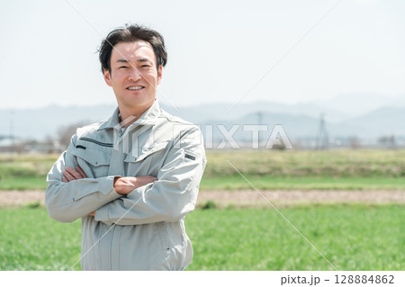 田舎の田んぼに立つ作業着姿のミドル世代の農家の男性 128884862