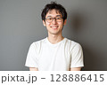 白いTシャツを着た若い日本人男性がグレーの背景の前で笑顔を見せるポートレート 128886415