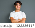 白いTシャツを着た若い日本人男性がグレーの背景の前で笑顔を見せるポートレート 128886417