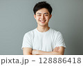 白いTシャツを着た若い日本人男性がグレーの背景の前で笑顔を見せるポートレート 128886418