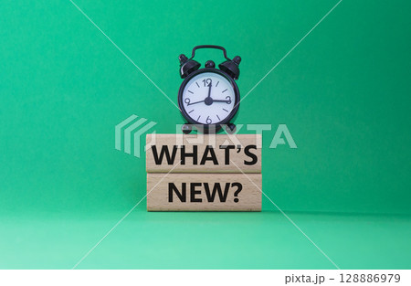 What is new symbol. Concept word What is new on wooden blocks. Beautiful green background with alarm clock. Business and What is new concept. Copy space 128886979