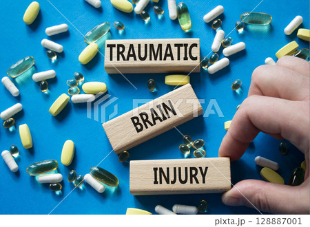 Traumatic Brain Injury symbol. Concept words Traumatic Brain Injury on wooden blocks. Beautiful blue background with pills. Doctor hand. Healthcare and Traumatic Brain Injury concept. Copy space. 128887001