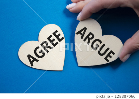 Agree or Argue symbol. Concept word Agree or Argue on wooden hearts. Businessman hand. Beautiful blue background. Business and Agree or Argue concept. Copy space 128887066
