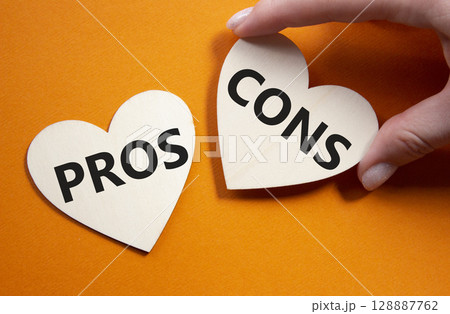 Pros vs Cons symbol. Concept word Pros vs Cons on wooden hearts. Businessman hand. Beautiful orange background. Business and Pros vs Cons concept. Copy space 128887762