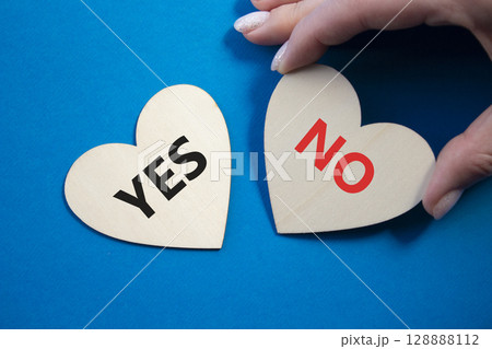 Yes or No symbol. Concept word Yes or No on wooden hearts. Businessman hand. Beautiful blue background. Business and Yes or No concept. Copy space Yes or No symbol. Concept word Yes or No on wooden hearts. Businessman hand. Beautiful blue background. Business and Yes or No concept. Copy space 128888112