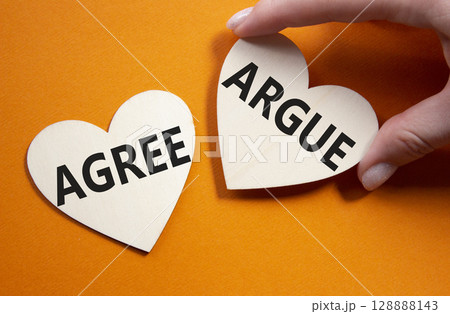 Agree or Argue symbol. Concept word Agree or Argue on wooden hearts. Businessman hand. Beautiful orange background. Business and Agree or Argue concept. Copy space Agree or Argue symbol. Concept word Agree or Argue on wooden hearts. Businessman hand. Beautiful orange background. Business and Agree or Argue concept. Copy space 128888143