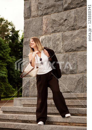 Smiling young woman joyfully descending outdoor stone staircase. Smiling young woman joyfully descending outdoor stone staircase. 128888341