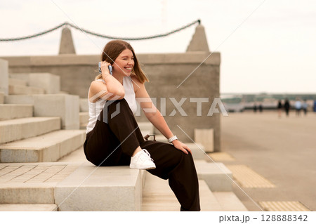 Young woman sitting on steps looking at phone outdoors in casual wear Young woman sitting on steps looking at phone outdoors in casual wear 128888342