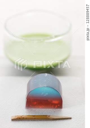 Cup of fresh matcha tea, green tea and Kingyoku can, traditional Japanese jelly confectionery on white wooden table. Cup of fresh matcha tea, green tea and Kingyoku can, traditional Japanese jelly confectionery on white wooden table. 128889457