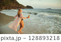 Woman walks on sunset on beach against background of sea. Girl i Woman walks on sunset on beach against background of sea. Girl i 128893218