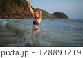 Woman stand knee-deep in sea on sunset. Girl on beach in green s Woman stand knee-deep in sea on sunset. Girl on beach in green s 128893219