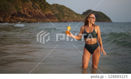 Woman stand knee-deep in sea on sunset. Girl on beach in green s 128893225