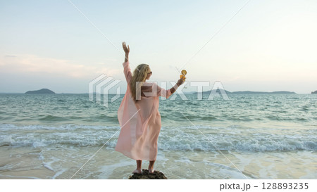 Woman stand on a reef rock stone in sea on sunset. Girl on beach Woman stand on a reef rock stone in sea on sunset. Girl on beach 128893235