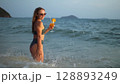Woman stand knee-deep in sea on sunset. Girl on beach in green s Woman stand knee-deep in sea on sunset. Girl on beach in green s 128893249