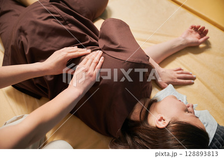 Masseuse making thai yoga massage. Cropped view of woman therapist doing traditional massage treatment for female patient. Client lying on mat, enjoying hand massage in calm atmosphere. Close up 128893813