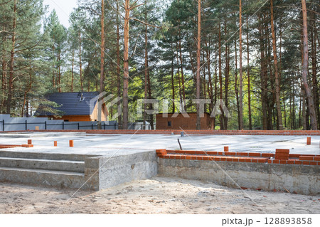 Concrete slab of foundation of house with laid pipes start of construction on project. Construction of cottages, design, engineering communications. Concrete slab of foundation of house with laid pipes start of construction on project. Construction of cottages, design, engineering communications. 128893858