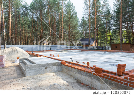 Concrete slab of foundation of house with laid pipes start of construction on project. Construction of cottages, design, engineering communications. Concrete slab of foundation of house with laid pipes start of construction on project. Construction of cottages, design, engineering communications. 128893873