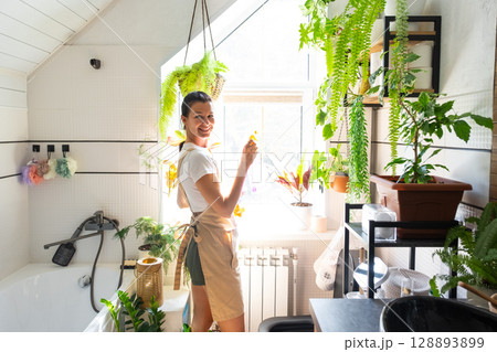 Portrait Woman in rubber gloves and apron manually cleaning in bathroom with rag cleaner and mop inside interior with home plants. Restoring order and cleanliness, cleaning servise Portrait Woman in rubber gloves and apron manually cleaning in bathroom with rag cleaner and mop inside interior with home plants. Restoring order and cleanliness, cleaning servise 128893899