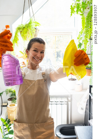 Portrait Woman in rubber gloves and apron manually cleaning in bathroom with rag cleaner and mop inside interior with home plants. Restoring order and cleanliness, cleaning servise 128893937