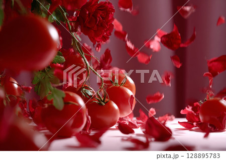 Surreal composition of tomatoes and roses with falling petals in dreamy red setting 128895783
