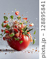 Exploding tomato in mid air with vibrant herbs and spices in slow motion 128895841
