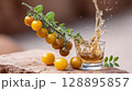 Golden cherry tomatoes with splash of liquid in glass on rustic surface 128895857