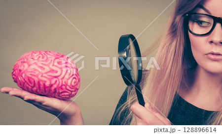 Woman holding magnifying glass investigating brain 128896614