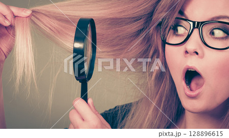 Woman holding magnifying glass looking at hair Woman holding magnifying glass looking at hair 128896615