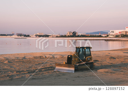 [タルイサザンビーチ]夕暮れ時の海辺とビーチを整備する重機 128897152