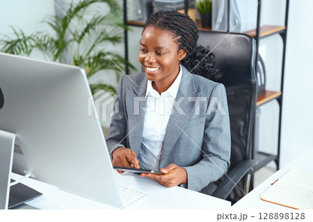 Professional Woman Smiling and Working at a Desk in a Modern Office Setting 128898128