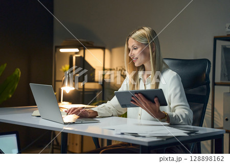 Professional Woman Working with Laptop and Tablet in a Modern Office Environment 128898162