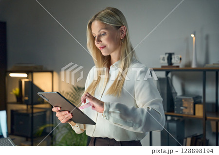 Professional Woman Using a Tablet in a Modern Office Setting at Night Professional Woman Using a Tablet in a Modern Office Setting at Night 128898194