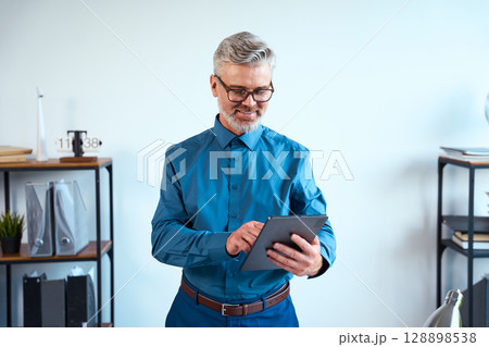 Confident Experienced Professional Using Digital Tablet in Modern Office Environment 128898538