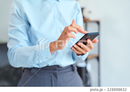 Professional Businesswoman Using Smartphone Indoors While Dressed in Formal Office Attire Professional Businesswoman Using Smartphone Indoors While Dressed in Formal Office Attire 128898632