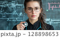 Young confident doctor woman holding stethoscope in front of medical charts background 128898653
