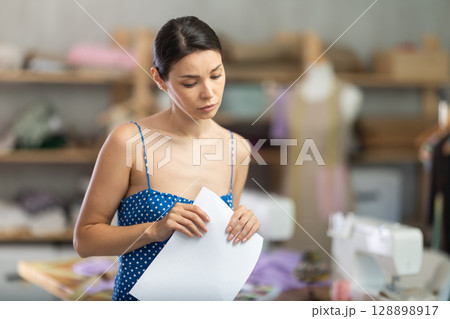 Upset woman seamstress with documents in workshop 128898917