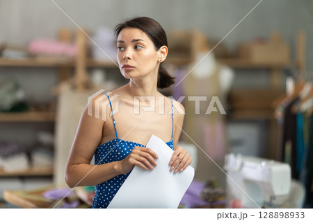 Upset woman seamstress with documents in workshop 128898933