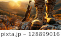 Hunter standing on rocks with rifle at sunset enjoying the view 128899016