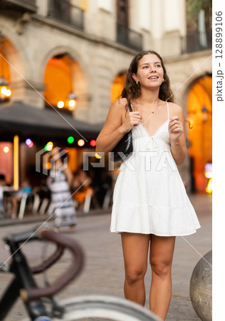 In evening, young smiling girl walks along city street Placa Real In evening, young smiling girl walks along city street Placa Real 128899106