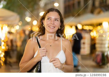 In evening, young smiling girl walks along city street La Rambla In evening, young smiling girl walks along city street La Rambla 128899198