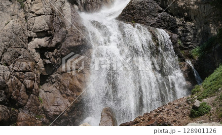 Powerful mountain waterfall cascading down rocky cliff face Powerful mountain waterfall cascading down rocky cliff face 128901126