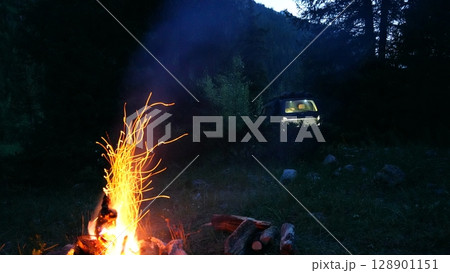Campfire burning brightly in wilderness with off road vehicle in background 128901151