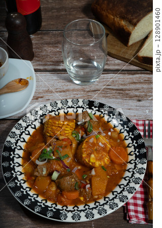 Hearty beef stew called carbonada with corn on the cob enjoyed with wine and bread 128901460