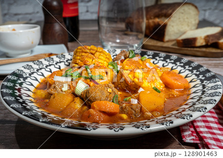 Hearty beef stew called carbonada with corn on the cob enjoyed with wine and bread 128901463